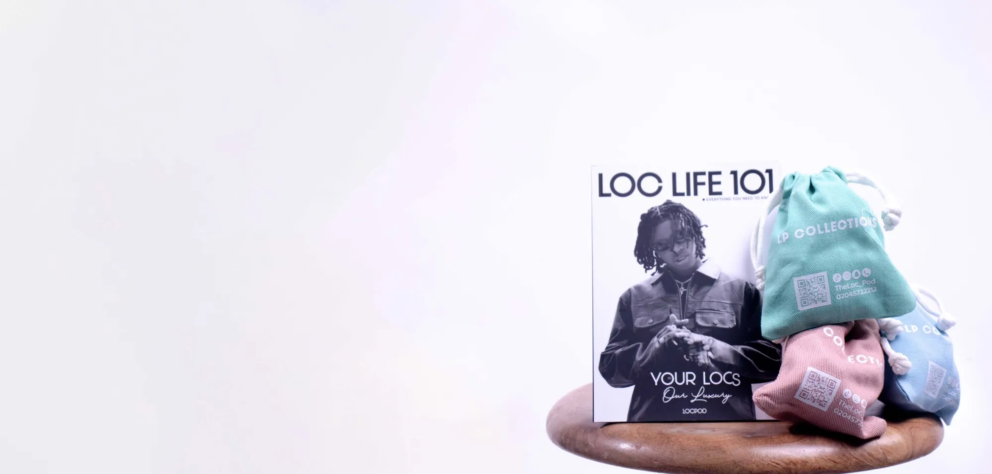 The Loc Life 101 magazine beside LP Collections drawstring bags on a wooden stool