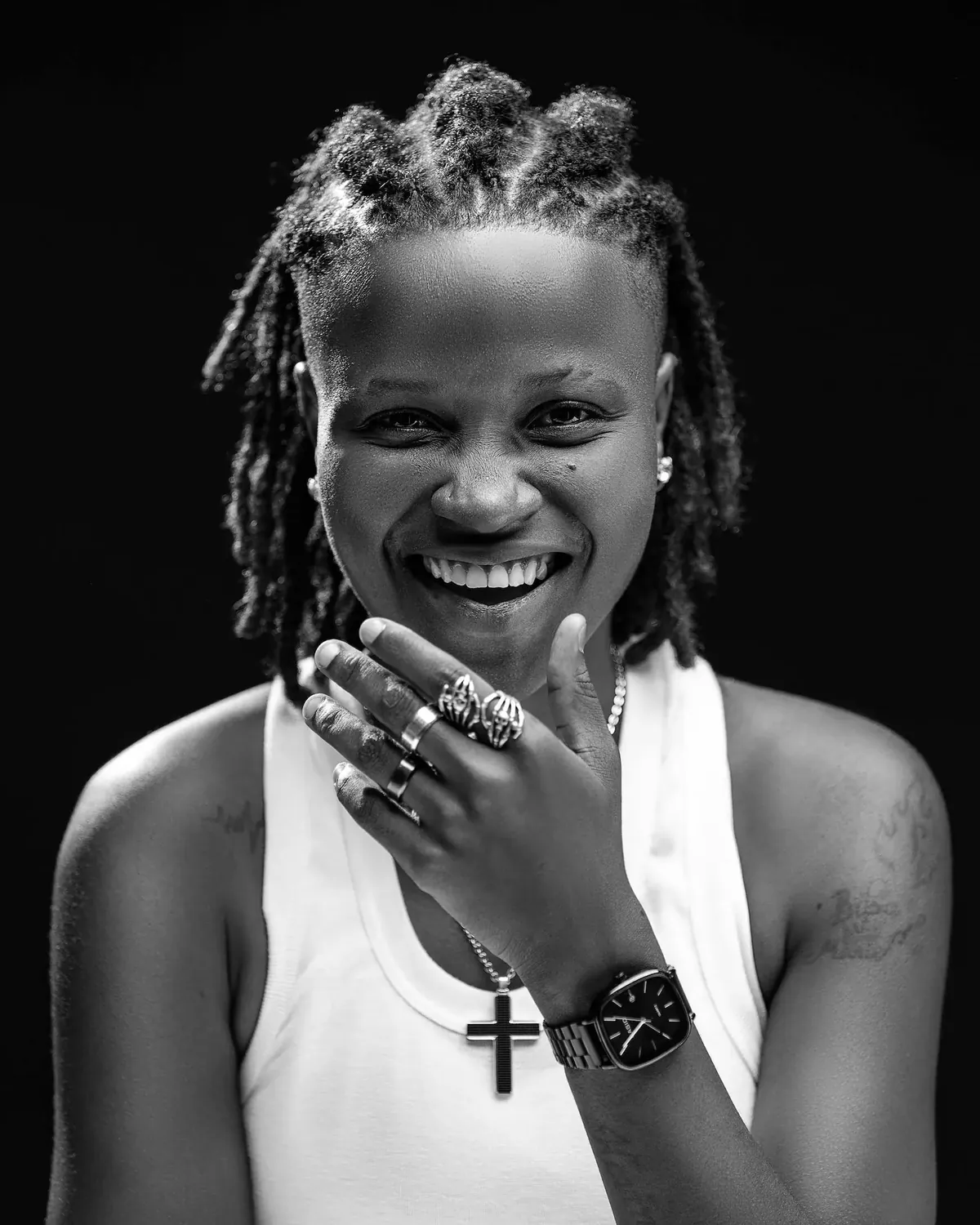 Black and white portrait of a smiling woman with short locs, hand to her chin